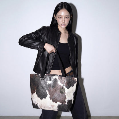 Model carrying the EMBER cow print Tyvek tote bag from the front