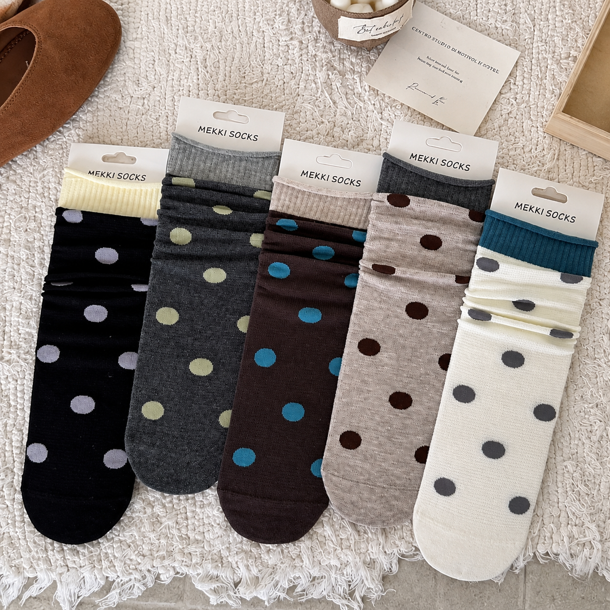 Five colorways of women's polka-dot slouch socks styled on a cream textured rug